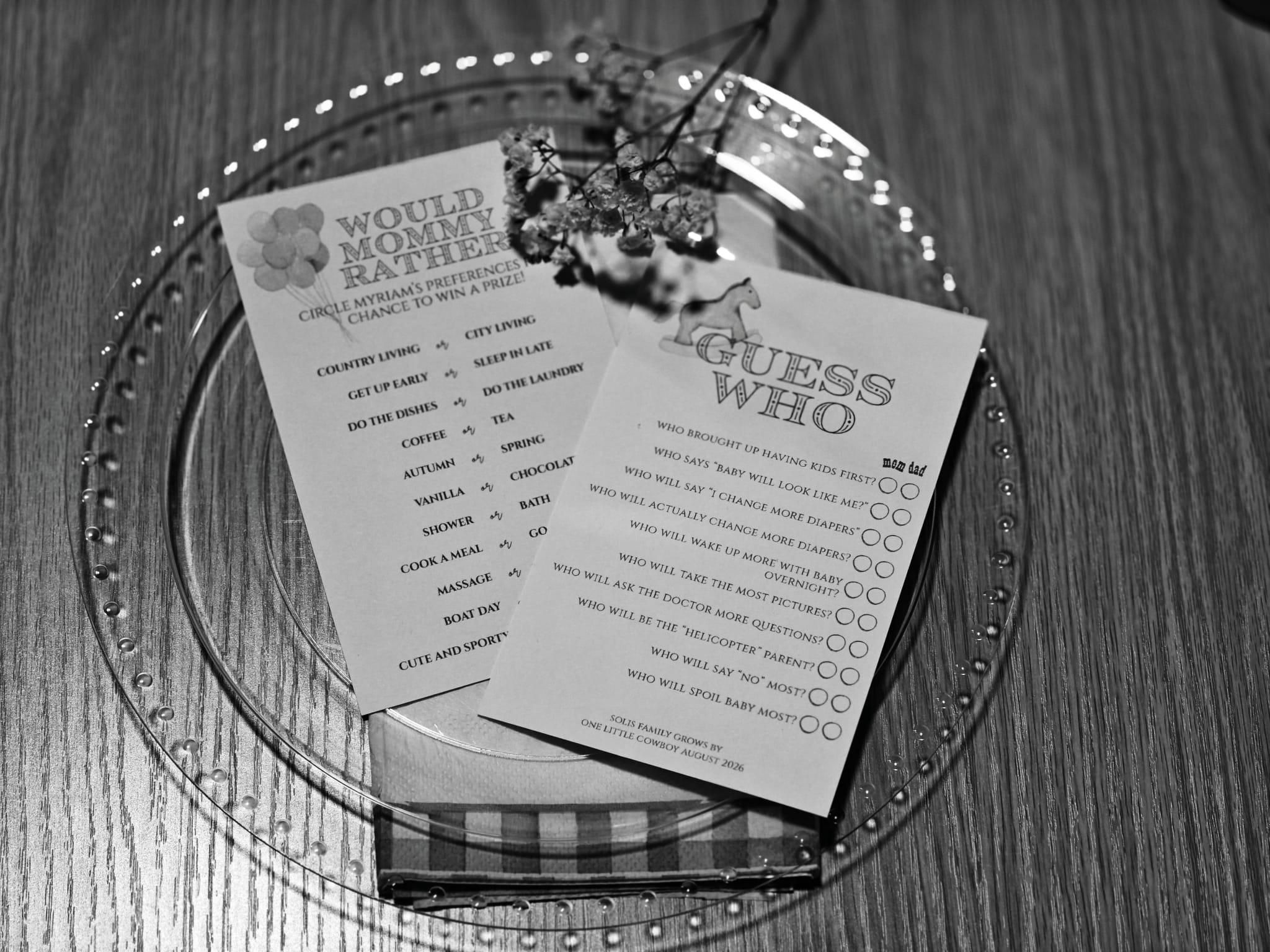 Overhead black-and-white photo of baby shower game cards on a beaded plate