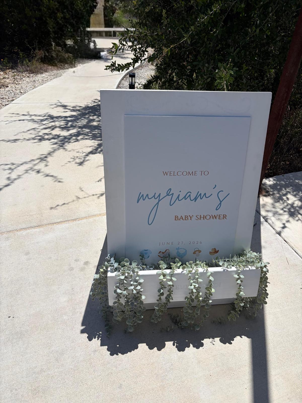 Freestanding welcome sign for a baby shower, framed on a garden pathway